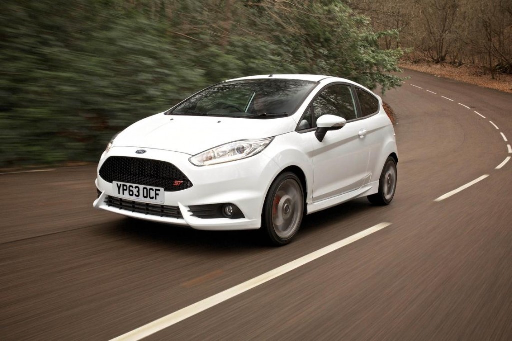 white compact car speeding round a country road bend