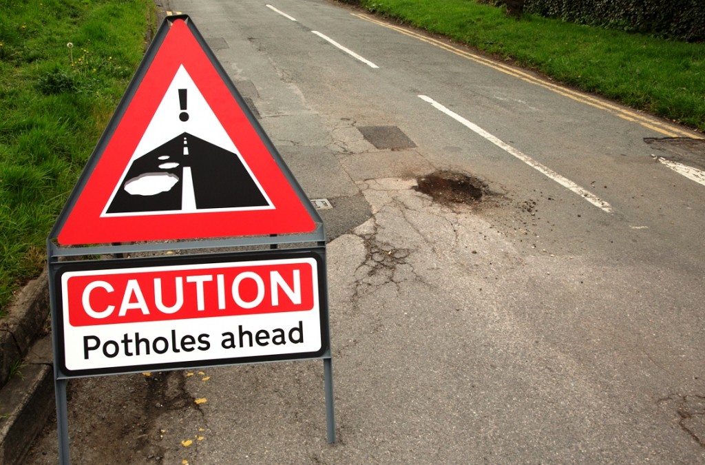 Potholes warning sign and road with pothole