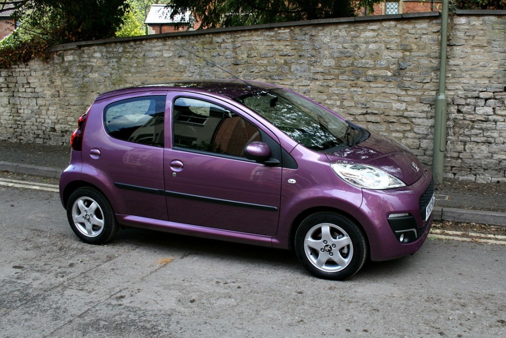 small aubergine-coloured car by a brick wall, side view