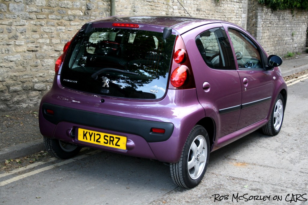 small aubergine-coloured car by a wall, back view